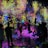 A vibrant and immersive digital art installation with bright, colorful light projections resembling flowers and abstract patterns covering the walls and floor. People are interacting with the environment, some sitting and others standing or walking around, creating an interactive and dynamic atmosphere.